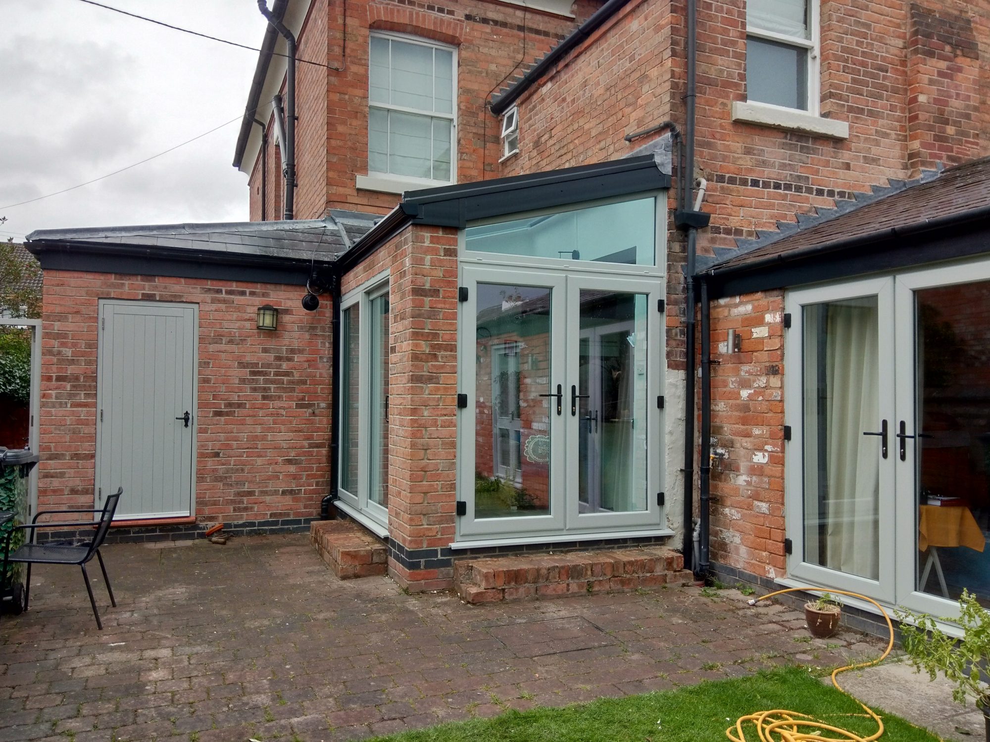 A wonderful gray Conservatory with matching windows and side door on a red brick house.